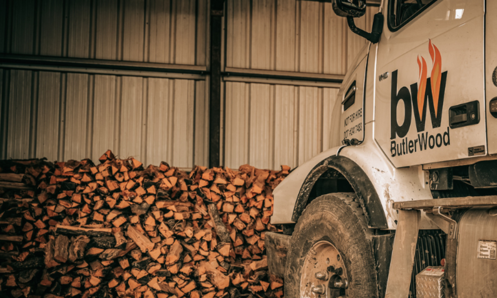A close up of a butlerwood truck in front of a wall of stacked firewood