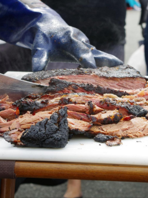 Close-up of sliced smoked meat on a white cutting board with a large blue glove covering one hand above the meat.