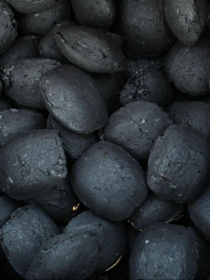 A close-up pile of dark charcoal or coke stones with a matte, textured gray-black surface.