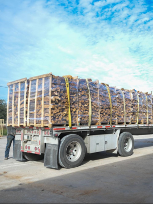 Truck carrying a large load of stacked wooden pallets on a clear day.