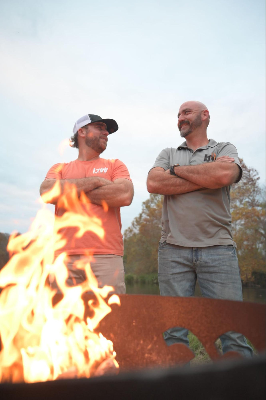 Austin and Jake Butler standing by a fire pit with flames and trees in the background