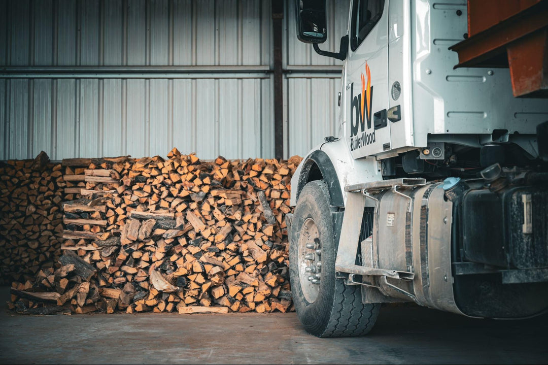 A Butlerwood truck in front of a large stack of firewood.