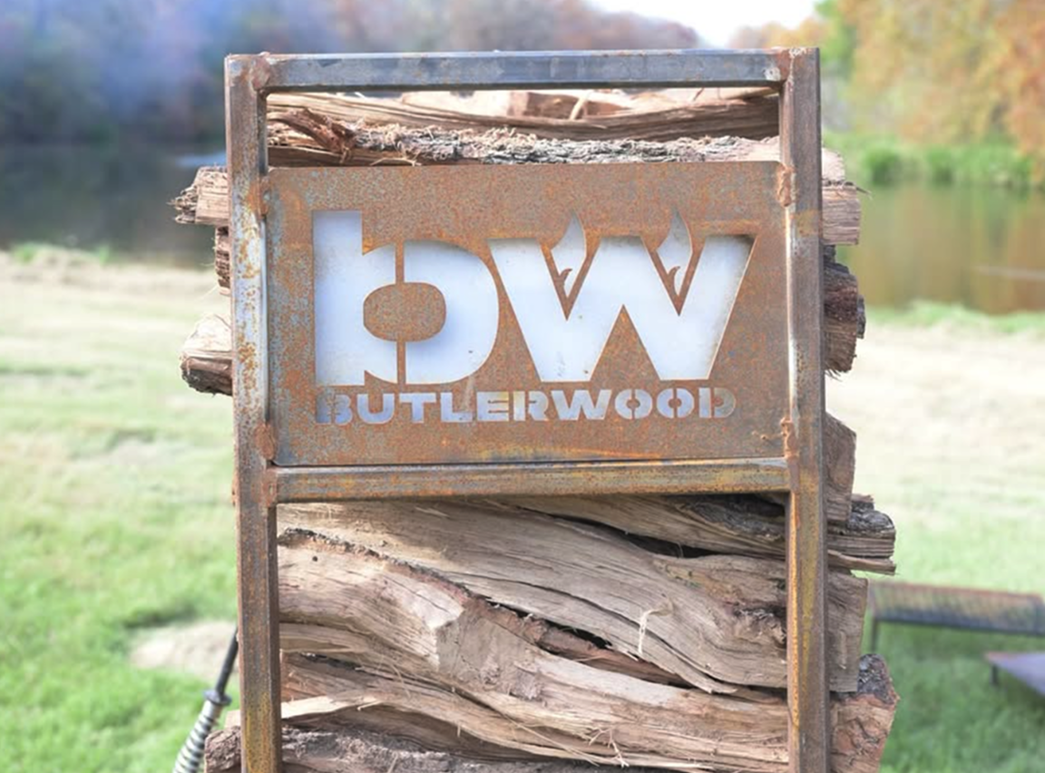 ButlerWood branded sign displayed outdoors in front of stacked wood.