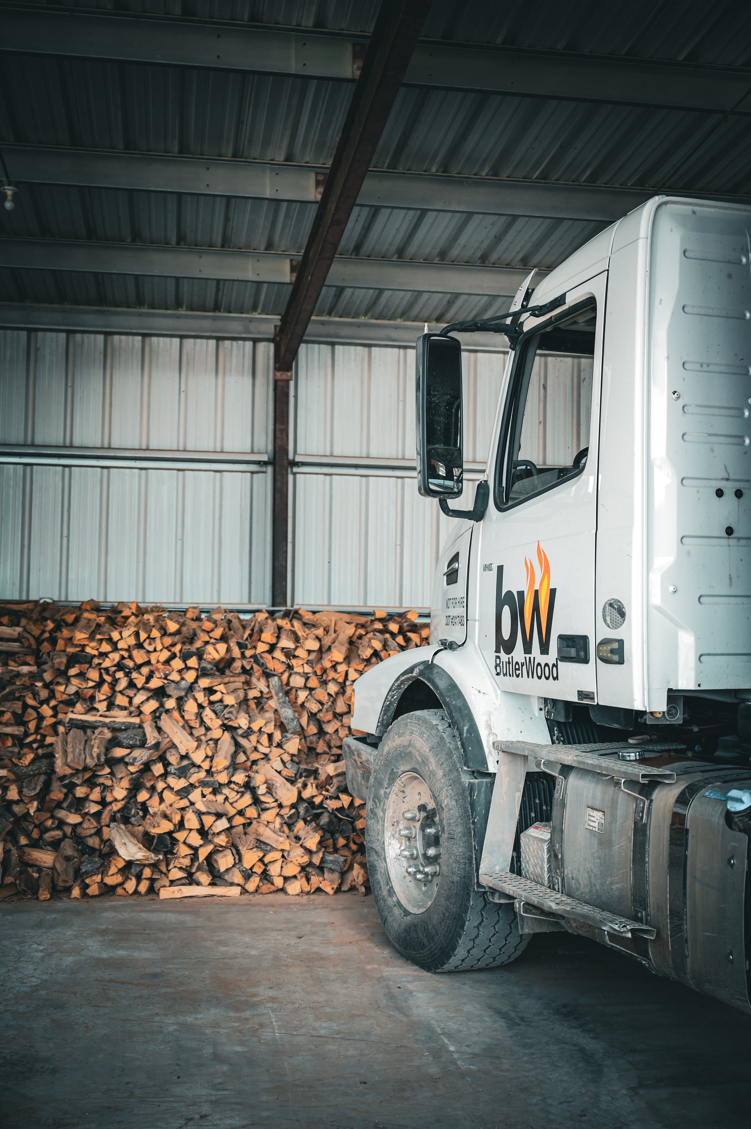 Truck with 'ButlerWood' logo parked next to stacked wood inside a warehouse.